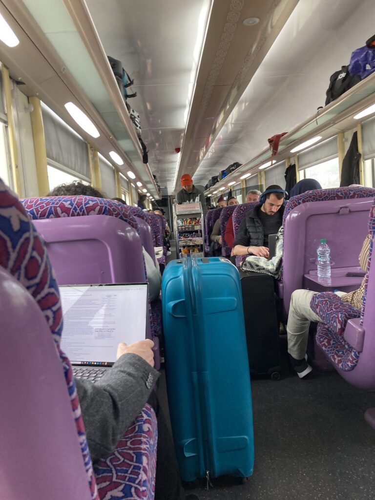 A scene inside the first class car with an attendant bringing a cart with beverages and snacks for sale.